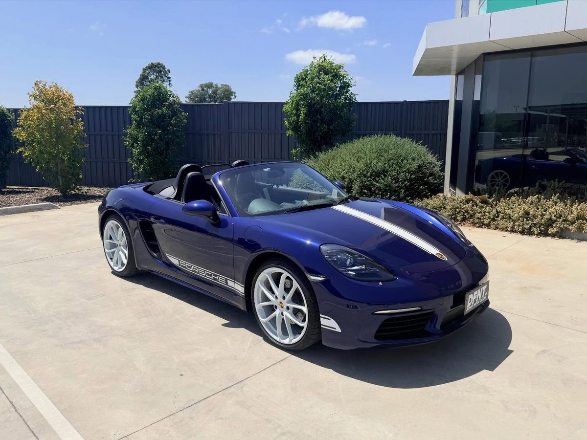 A dark blue Porsche 718 Boxster finished outside the workshop, white bonnet stripe and white wheels