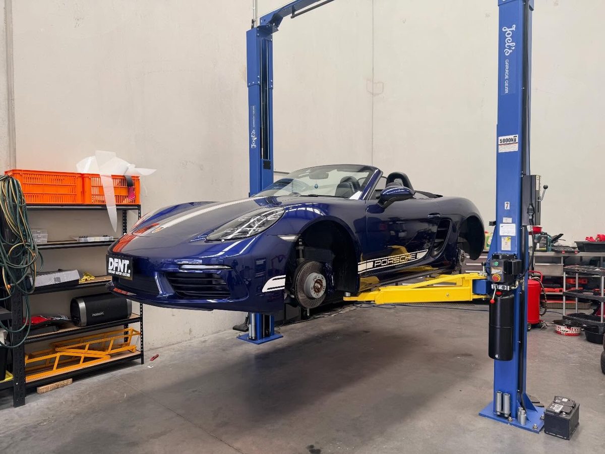 The blue Porsche 718 up on the hoist with the wheels off, stripes and side decals going on