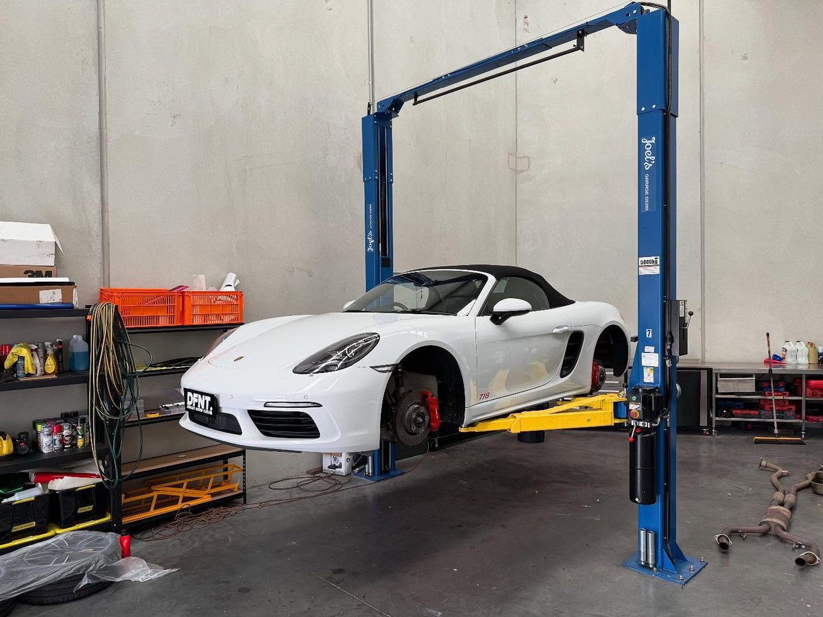 A white Porsche 718 Boxster up on the hoist with the wheels off