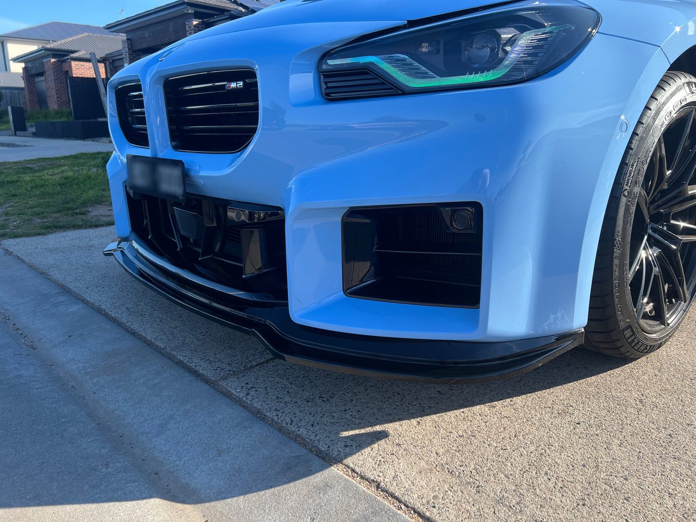 Front end of a light blue BMW M2 with a gloss black front lip and blacked-out grille surrounds